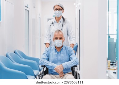 Middle aged female doctor carrying senior man patient in wheelchair wearing face protective medical mask for protection from virus disease at hospital corridor. Health safety and pandemic concept. - Powered by Shutterstock