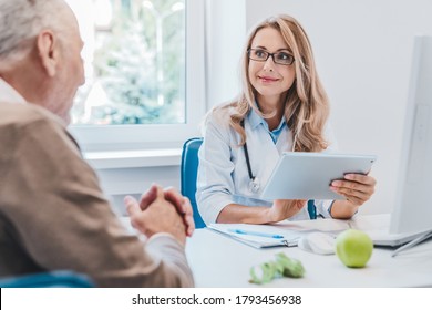 Middle Aged Female Doctor Nutritionist In White Medical Coat Consulting Her Old Patient Using Digital Tablet