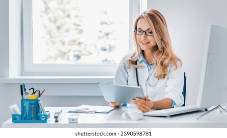 Middle aged female doctor sitting at desk and using digital tablet in office. Telemedicine. General practitioner family doctor gynecologist checking on diagnosis, sending test results online - Powered by Shutterstock