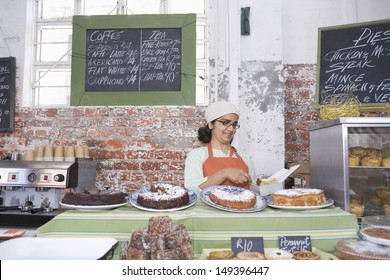 Middle Aged Female Owner Working At Counter In Cake Shop