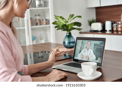 Middle Aged Female Patient Getting Online Telemedicine Consultation At Home. Male Doctor Consulting Senior Old Woman By Telehealth Video Call Virtual Healthcare Visit On Laptop. Over Shoulder View