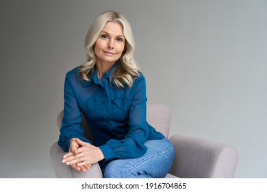 Middle aged female psychotherapist, counselor sitting in chair alone in office looking at camera. Sophisticated elegant mature 50s woman of mid age with blond hair posing indoors, portrait. - Powered by Shutterstock