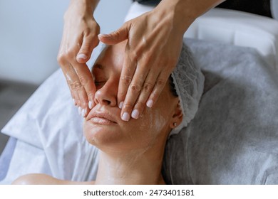 Middle aged female receiving facial massage in beauty salon. Anti aged massage and skincare concept with a beautiful woman. Hands of cosmetology specialist making facial lifting massage in SPA salon - Powered by Shutterstock