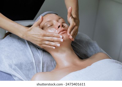 Middle aged female receiving facial massage in beauty salon. Anti aged massage and skincare concept with a beautiful woman. Hands of cosmetology specialist making facial lifting massage in SPA salon - Powered by Shutterstock