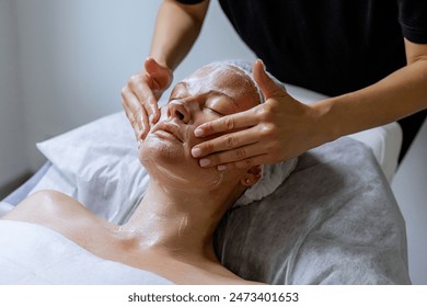 Middle aged female receiving facial massage in beauty salon. Anti aged massage and skincare concept with a beautiful woman. Hands of cosmetology specialist making facial lifting massage in SPA salon - Powered by Shutterstock