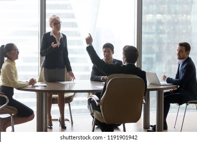 Middle Aged Female Team Leader Stand Listening To Colleagues Ideas At Briefing, Diverse Employee Brainstorm Expressing Thoughts To Coworkers, Negotiating At Office Business Meeting. Teamwork Concept