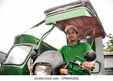 A middle aged Filipino tricycle driver in a green tricycle parked by the road.