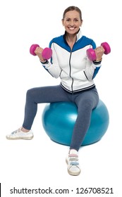 Middle Aged Fit Woman Exercising While Sitting On A Fitness Ball With Dumbbells.