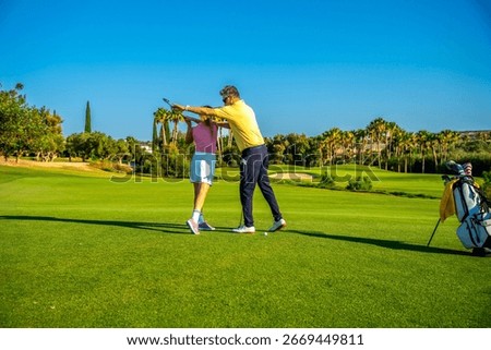 Middle aged golf instructor assisting young woman golfer on improving her swing on a sunny day at the golf course