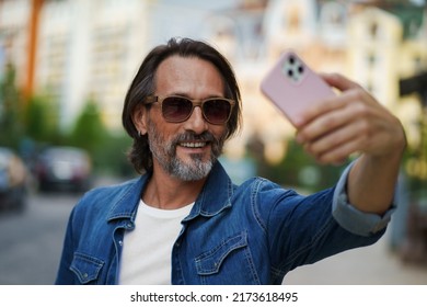 Middle Aged Handsome Grey Bearded Metrosexual Man Smiling On Camera Old Town Wearing Casual. Happy Senior Man On Street Of European City Making Selfie Using Mobile Phone. Travel Concept. 