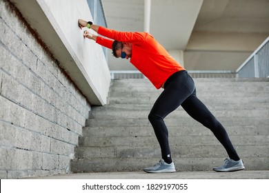 Middle aged handsome runner in shape doing warmup exercises on stairs.