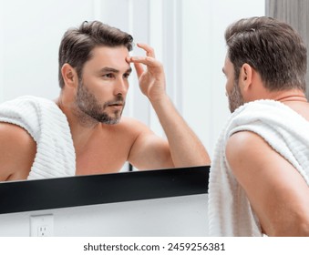 Middle aged hispanic man looking in mirror, facial skin and stubble. Male beauty care product. Skincare, home spa. Beauty portrait of a beautiful man. Spa model, moisturizing nourishing creme. - Powered by Shutterstock