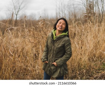 Middle Aged Laughing Asian Woman Laughing On Cold Autumn Day In Midwest; Tall Dry Grass In Background