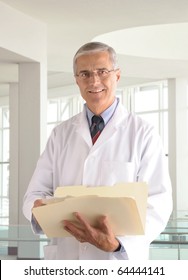 Middle Aged Male Doctor In Lab Coat Holding A Manila Folder In Modern Medical Office Setting.