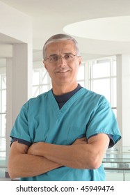 Middle Aged Male Doctor In Scrubs With Arms Folded In Modern Office Setting Vertical Format