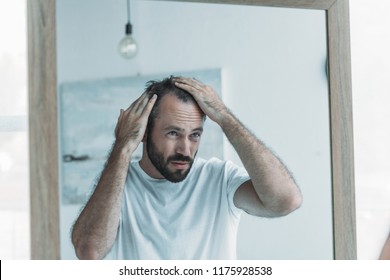 middle aged man with alopecia looking at mirror, hair loss concept 