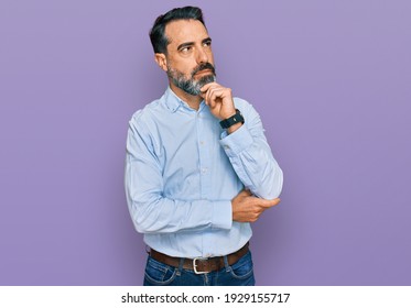 Middle aged man with beard wearing business shirt with hand on chin thinking about question, pensive expression. smiling with thoughtful face. doubt concept. 