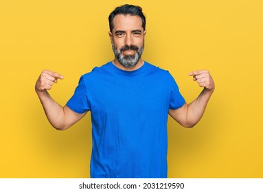 Middle aged man with beard wearing casual blue t shirt looking confident with smile on face, pointing oneself with fingers proud and happy. 