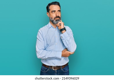 Middle aged man with beard wearing business shirt with hand on chin thinking about question, pensive expression. smiling and thoughtful face. doubt concept. 