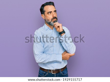 Middle aged man with beard wearing business shirt with hand on chin thinking about question, pensive expression. smiling with thoughtful face. doubt concept. 