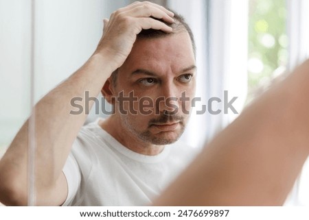 Middle aged man checking his bald spots in the mirror, hair loss concept