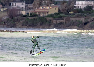 A middle aged man is doing some foil surfing or hydrofoil surfing in the sea, with a paddle in his hands. 