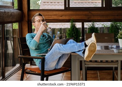 Middle aged man drinks wine while watching online broadcast on laptop sitting on the veranda of his country house - Powered by Shutterstock