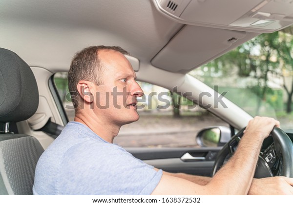 Middle aged\
man driving the car with attention at the road and fastened seat\
belt. Safe driving concept, color\
image.