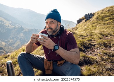 Middle aged man enjoying a hot drink while resting during a mountain hiking trip - Powered by Shutterstock