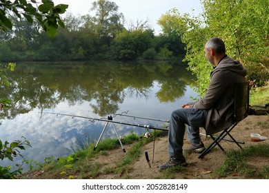 A Middle Aged Man Fishing For Carp On A Side Of A Pond On An Autumn Morning.