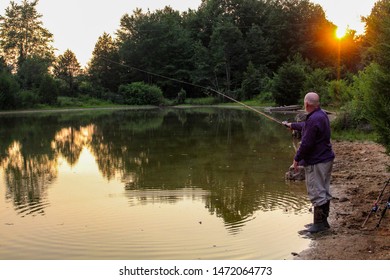 Middle Aged Man Fishing At Sunset On A Serene Country Pond In The Summertime