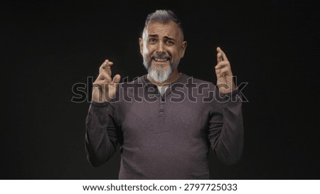 Middle aged man with hands pressed together in a black studio, palms touching and pleading expression, bare hands visible; pleading apology.