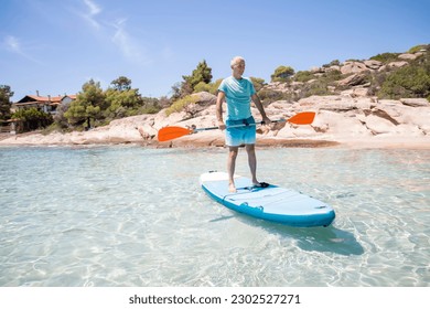 Middle aged man having fun, standing with a paddle on a board in the water. SUP. Standup paddle boarding in summer - Powered by Shutterstock