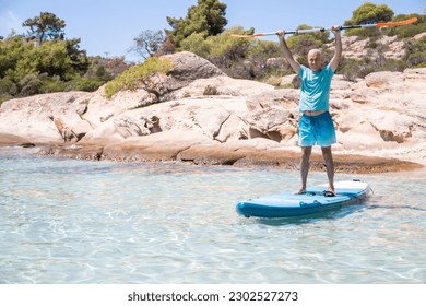 Middle aged man having fun, standing with a paddle on a board in the water. SUP. Standup paddle boarding in summer - Powered by Shutterstock