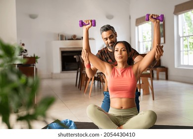 Middle Aged Man Helping Ethnic Woman Working With Dumbbells At Home. Black Fit Woman With Her Personal Fitness Trainer Exercising With Weights. Multiethnic Girl Doing Chest And Shoulder Dumbbell Press