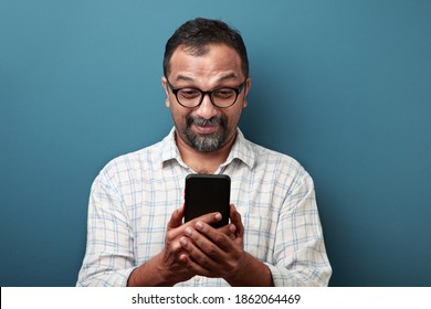 Middle Aged Man Of Indian Origin Looking At His Mobile Phone With A Surprise