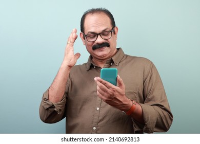 Middle Aged Man Of Indian Origin With A Communicative Gesture Looks At His Mobile Phone