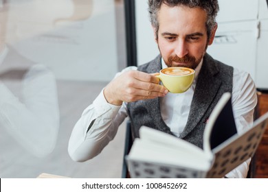 Middle aged man jewish nationality spends afternoon or morning in trendy or hipster coffee shop, sips on coffee while reading book. Competely immersed and interested in content of article - Powered by Shutterstock