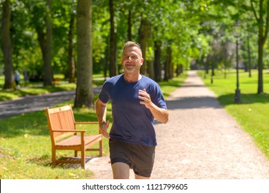 Middle Aged Man Jogging Along Alley In Park On Sunny Day In A Close Up View