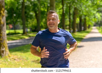 Middle Aged Man Jogging Along Alley In Park On Sunny Day In A Close Up Cropped View