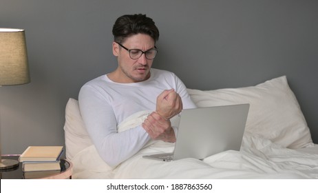 Middle Aged Man With Laptop Having Wrist Pain In Bed