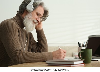 Middle Aged Man With Laptop And Headphones Learning At Table Indoors