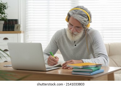 Middle Aged Man With Laptop, Notebook And Headphones Learning At Table Indoors