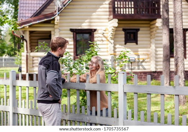 Middle aged man meeting\
smiling female neighbor in countryside and talking cheerfully to\
her over fence