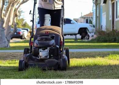 Middle Aged Man Mowing An Overgrown Lawn In The Afternoon Sun In The Winter.  San Mateo, California