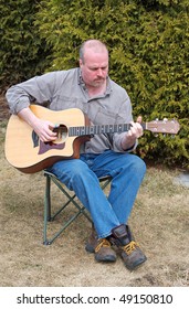 A Middle Aged Man Plays His Guitar Outside On A Nice Spring Day.