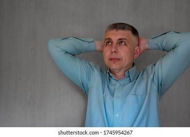 Middle Aged Man Portrait With Crossed Hands Behind His Head. 40 Years Man Not Looking At Camera. Blue Business Shirt Is Dressed. Thinking Face And Calm Emotions