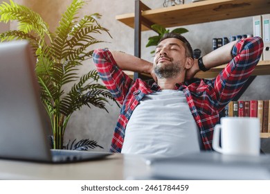 Middle aged man resting in front of laptop screen at his work place, with arms behind the head. Millennial freelancer worker leaning back at workplace, enjoying his job, feeling pleased and satisfied - Powered by Shutterstock