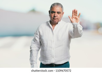 Middle aged man serious and determined, putting hand in front, stop gesture, deny concept