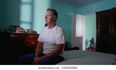 Middle aged man sitting by bed looking at camera in authentic real life domestic lifetyle scene of older person in bedroom solitude - Powered by Shutterstock